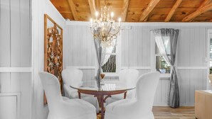 A dining area with a round table, white chairs, a chandelier, and wooden ceiling beams.