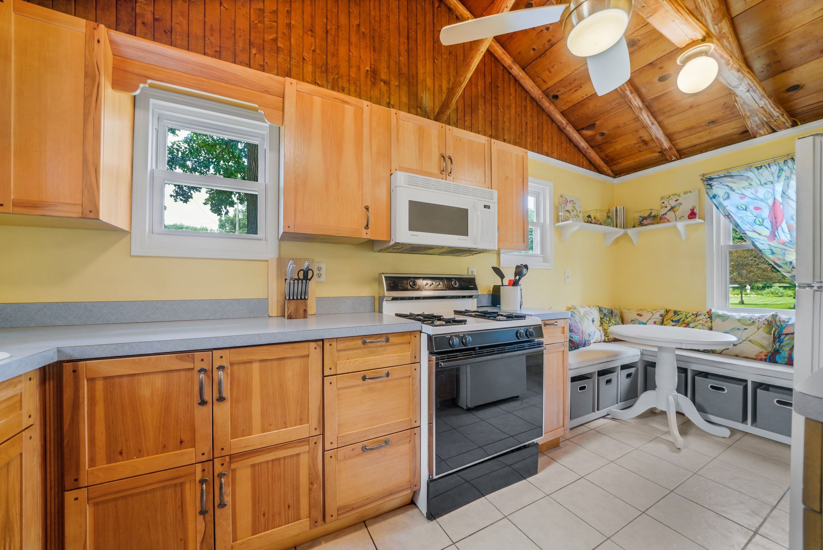 A kitchen with wooden cabinets, a microwave, stove, oven, and a window with a view of trees.