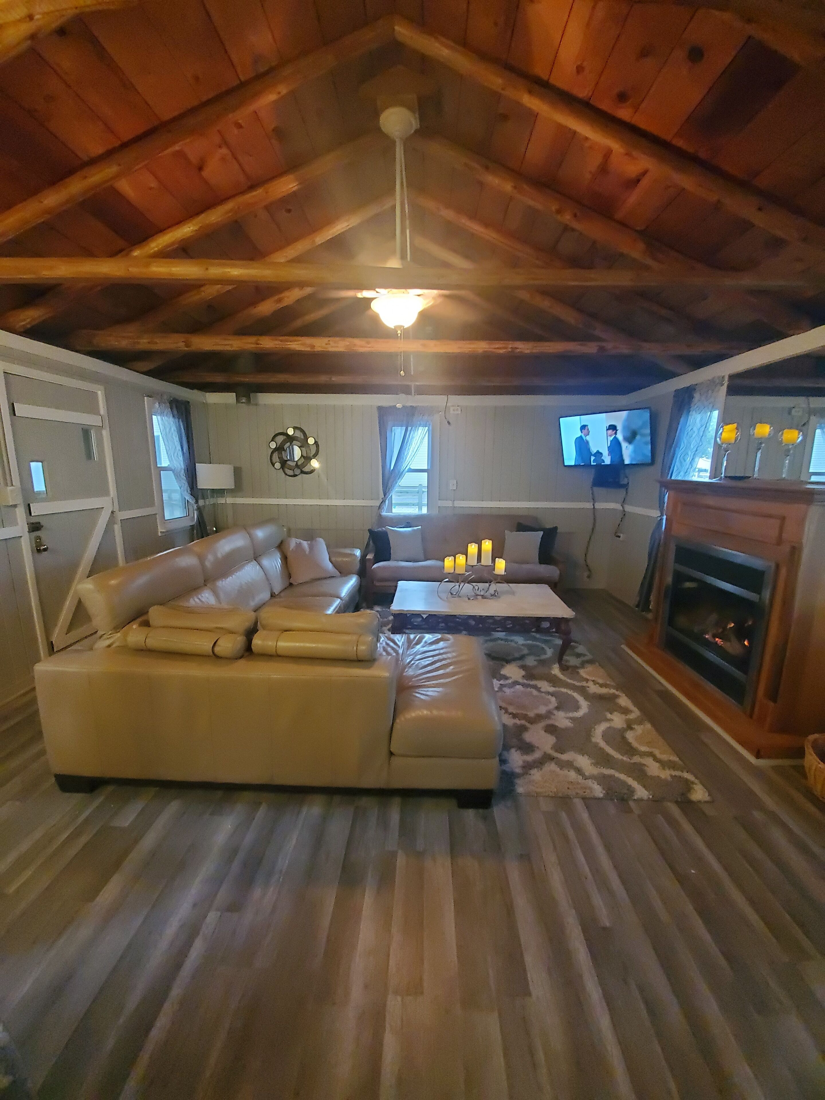 A cozy living room with a wooden ceiling, a sectional sofa, a coffee table, a fireplace, and a television.