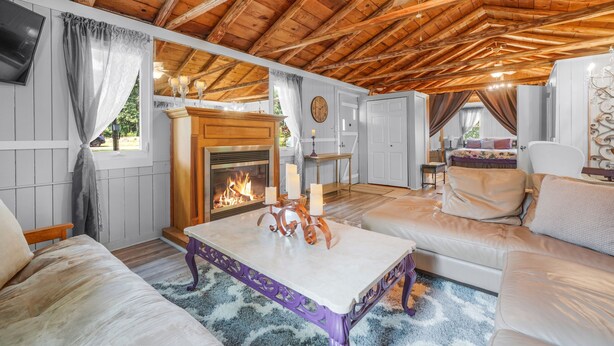 A cozy cabin interior with a wooden ceiling, a fireplace, a sofa, and a dining area.