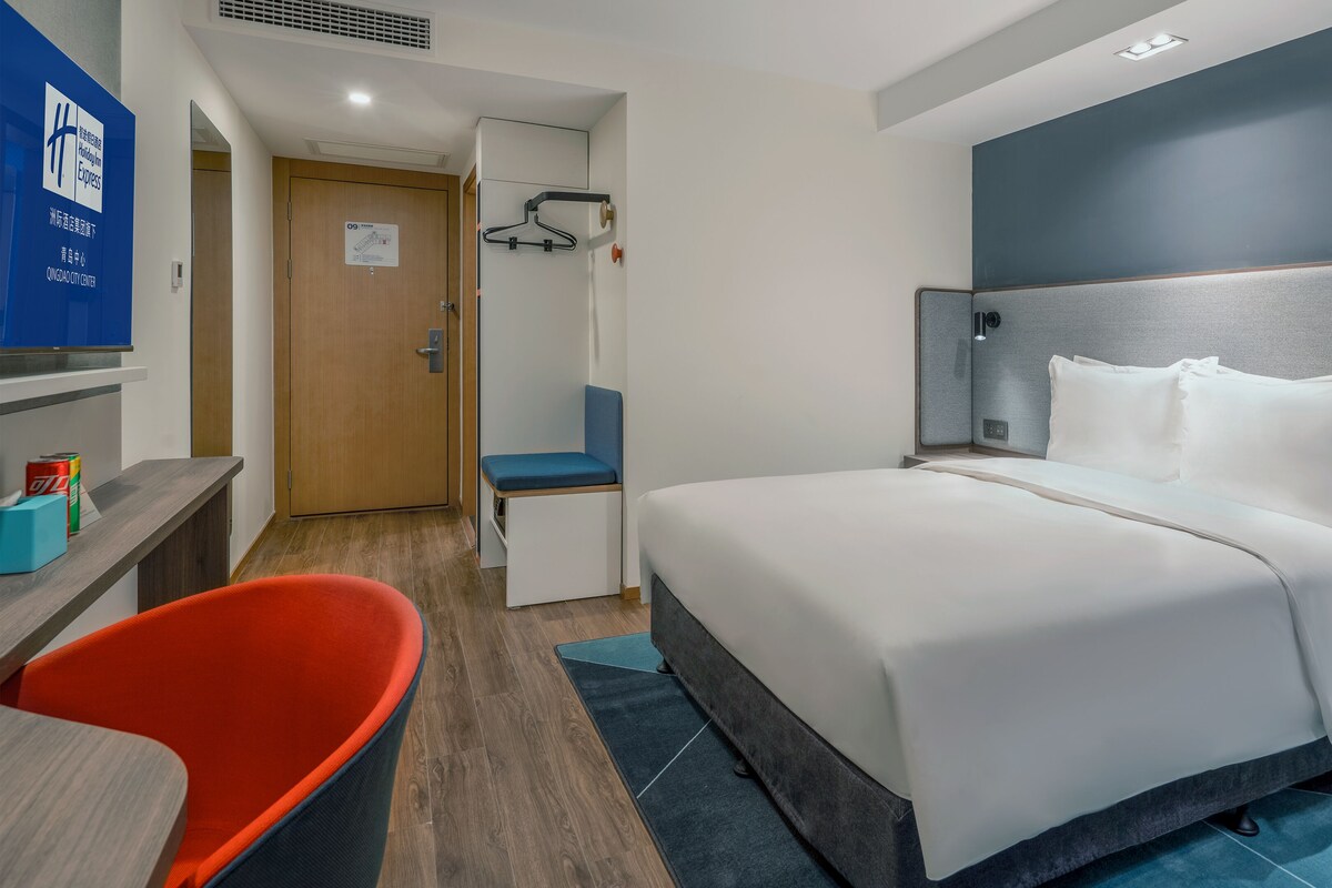 A hotel room with a bed, a desk, a chair, and a wardrobe.