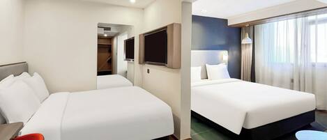 A hotel room with two beds, a TV, a desk, and a window with curtains.