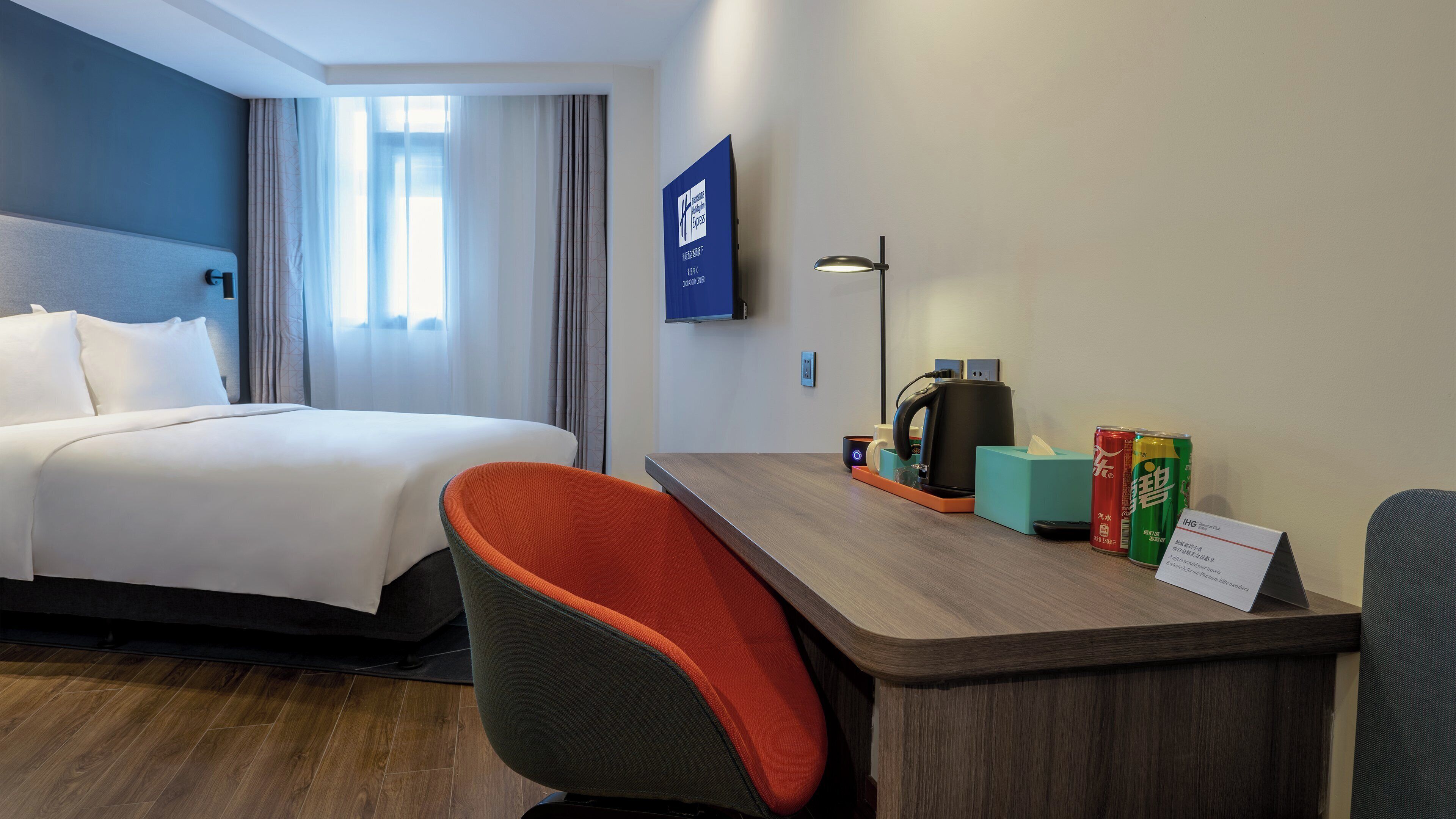 A hotel room with a bed, a desk with a chair, a coffee maker, and a sign indicating the room type.