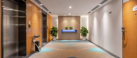 A modern elevator with a stainless steel finish, a reception desk with a blue illuminated panel, and a patterned carpet.