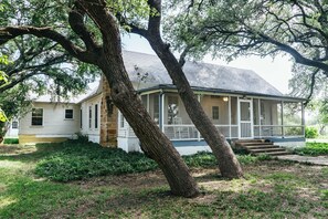 A two-story house with a porch and a large tree in front.