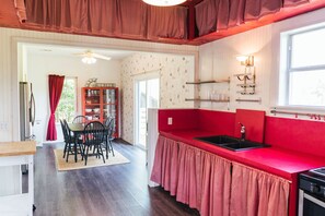 A kitchen with red countertops, a black sink, and a window. There is a dining area with a table and chairs.