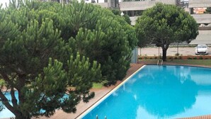 A swimming pool with a wooden deck, surrounded by a fenced area with trees. - Apartment with view and pool access 900 meters from the beach (Ovar)