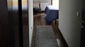 A narrow hallway leading to a bedroom with a bed, a radiator, and a window. - Apartment with view and pool access 900 meters from the beach (Ovar)