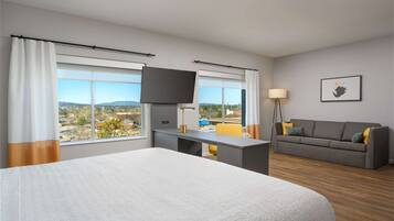 Habitación de hotel con una cama grande, un escritorio, un televisor de pantalla plana, un sofá y vistas a la ciudad.