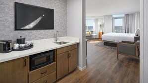 Una habitación de hotel moderna con área de cocina, cama y vista a la ciudad.