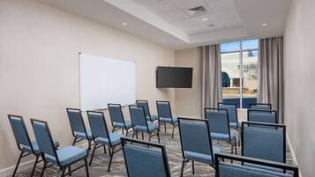 Un salón de conferencias con filas de sillas azules, una pizarra y un televisor en la pared.