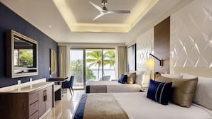 Habitación de hotel con una cama grande, un escritorio, una silla, un televisor y vistas a palmeras.