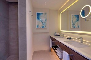 A modern bathroom with two sinks, a large mirror with a light, and abstract art on the wall. - Royalton Grenada (St. George's)