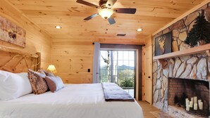 A wooden cabin bedroom with a bed, a stone fireplace, and a ceiling fan. - Stunning Views over Aska +Hot Tub & Firepit +Arcade and Pool table +Near Toccoa (Blue Ridge)