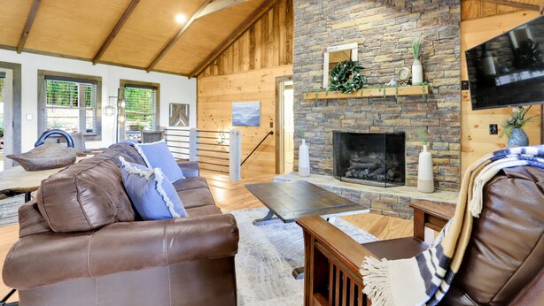 A cozy living room with a stone fireplace, leather sofa, and wooden ceiling beams. - Stunning Views over Aska +Hot Tub & Firepit +Arcade and Pool table +Near Toccoa (Blue Ridge)