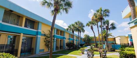 A hotel with a row of rooms, palm trees, and a clear sky.