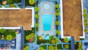 Vue aérienne d’un hôtel doté d’une piscine centrale, entourée d’espaces paysagers et de sentiers.