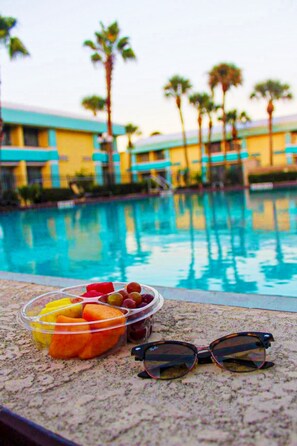 Una piscina con una vista despejada del área a su alrededor, un cuenco de frutas variadas y un par de gafas de sol en el borde de la piscina.