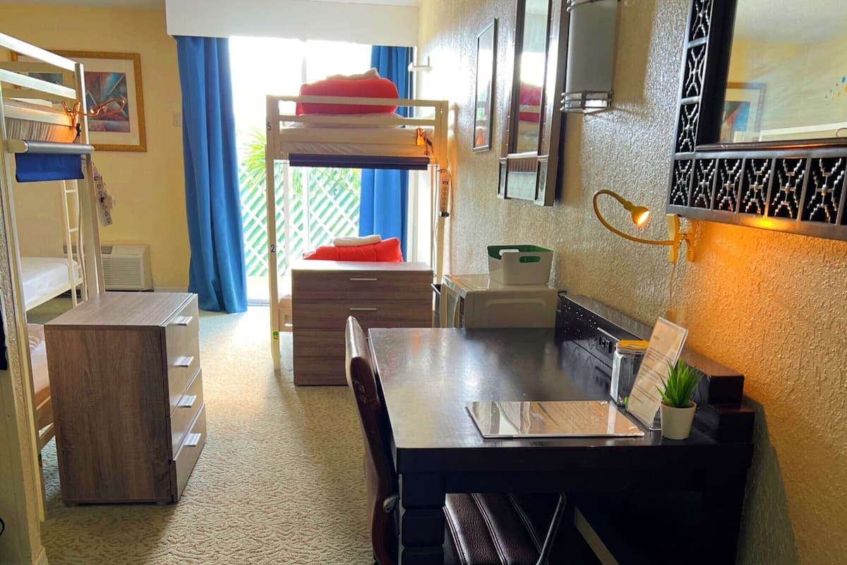 A compact room with bunk beds, a desk, and a kitchenette.