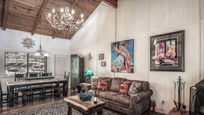 A spacious living room with a wooden ceiling, a chandelier, a dining area with a table and chairs, and a large painting on the wall. - A Climbing Cub by Ruidoso Vacation Rentals (Ruidoso)