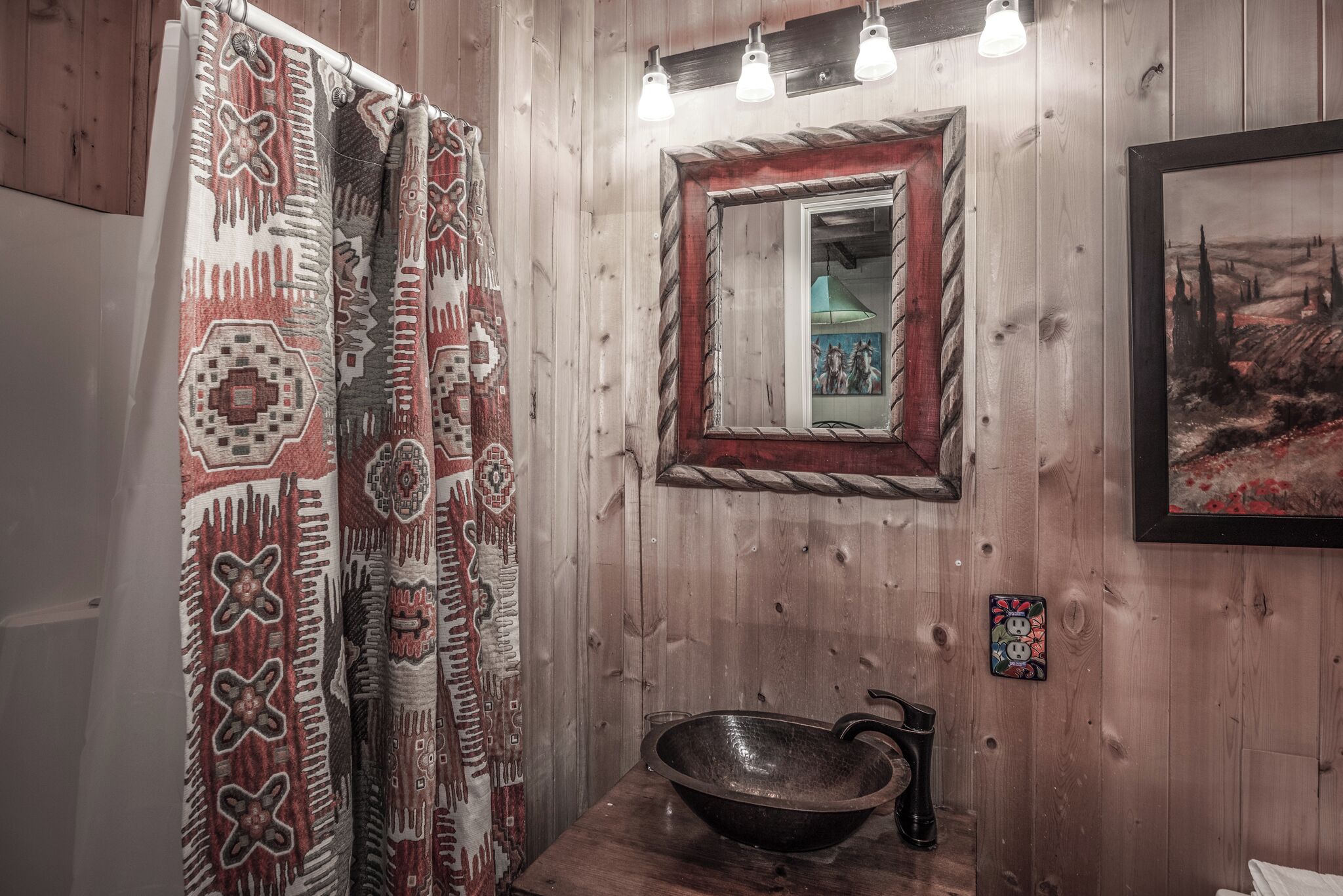 Une salle de bain en bois au décor rustique, comprenant un grand lavabo, un miroir avec un cadre rouge et des rideaux à motifs.
