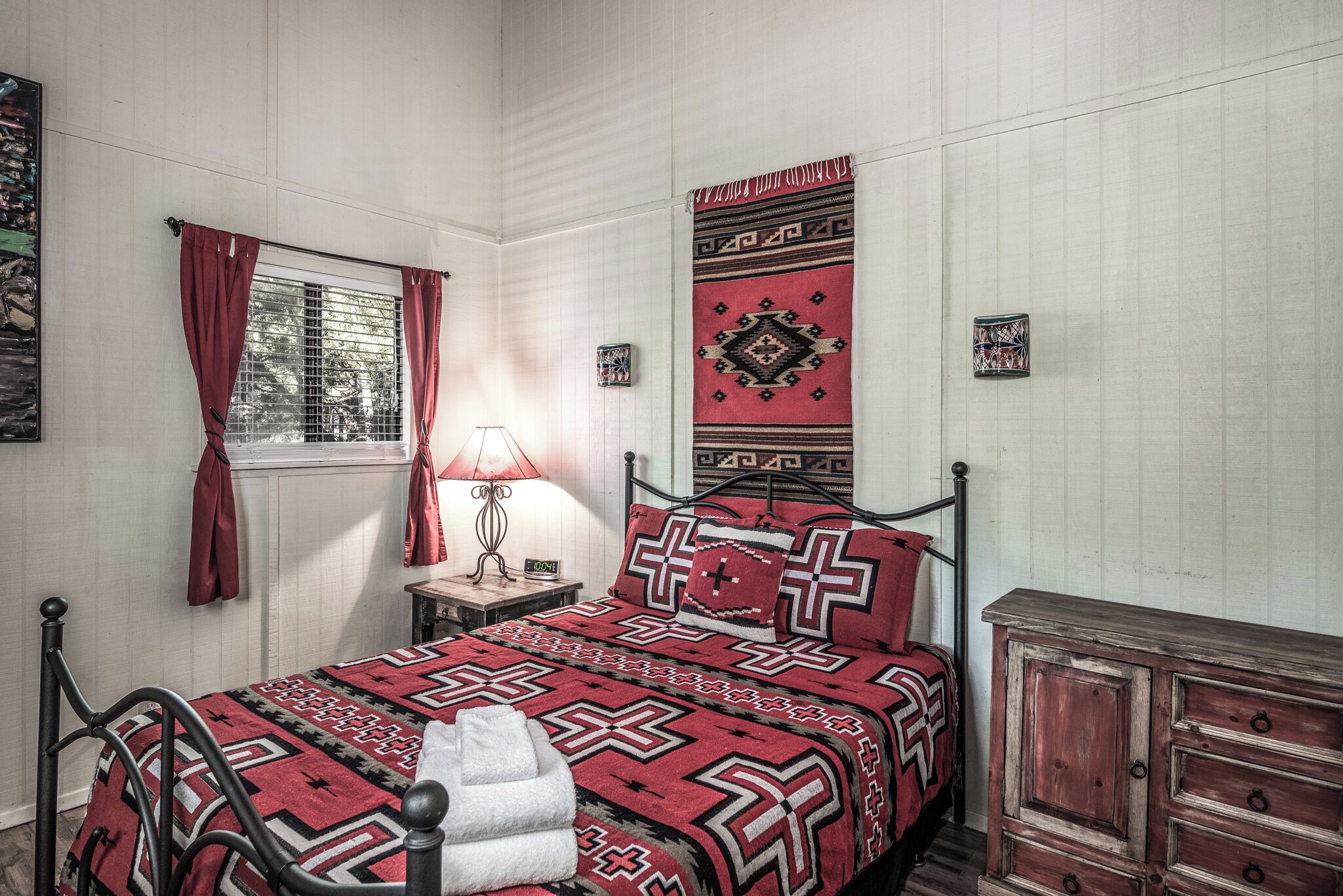 Quarto bem arrumado com cama, mesa de cabeceira, abajur e cômoda.