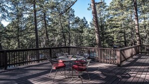 A wooden deck with a round table and chairs, surrounded by a wooden railing, overlooking a forested area. - A Climbing Cub by Ruidoso Vacation Rentals (Ruidoso)