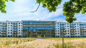 Un edificio residenziale a più piani con balconi, un ingresso centrale e uno sfondo sabbioso.