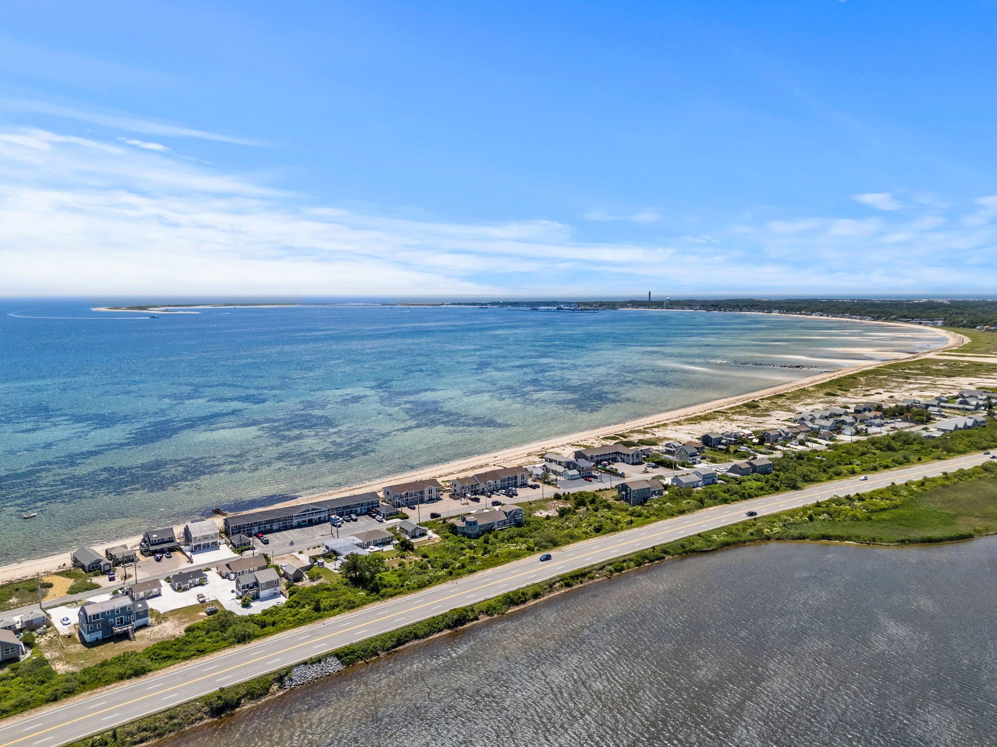 Une vue aérienne d’un quartier résidentiel situé sur la côte, avec des maisons le long de la plage, une route parallèle au rivage et une vue dégagée sur l’océan.