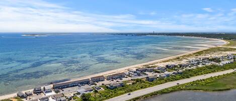 Une vue aérienne d’un quartier résidentiel situé sur la côte, avec des maisons le long de la plage, une route parallèle au rivage et une vue dégagée sur l’océan.