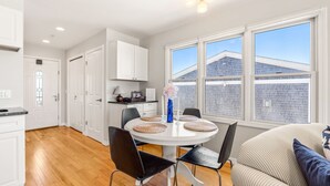 Una cocina moderna con armarios blancos, una mesa redonda de comedor con sillas negras y un ventanal con vista a una casa.