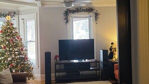 Een woonkamer met een kerstboom, een flatscreen televisie en een open haard.