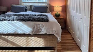 Een slaapkamer met een bed, een plafondventilator, een raam met zonwering, een nachtkastje met een lamp en een kledingkast.