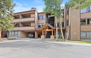 A multi-story building with a covered entrance, stone pillars, and a vehicle parked in the driveway.