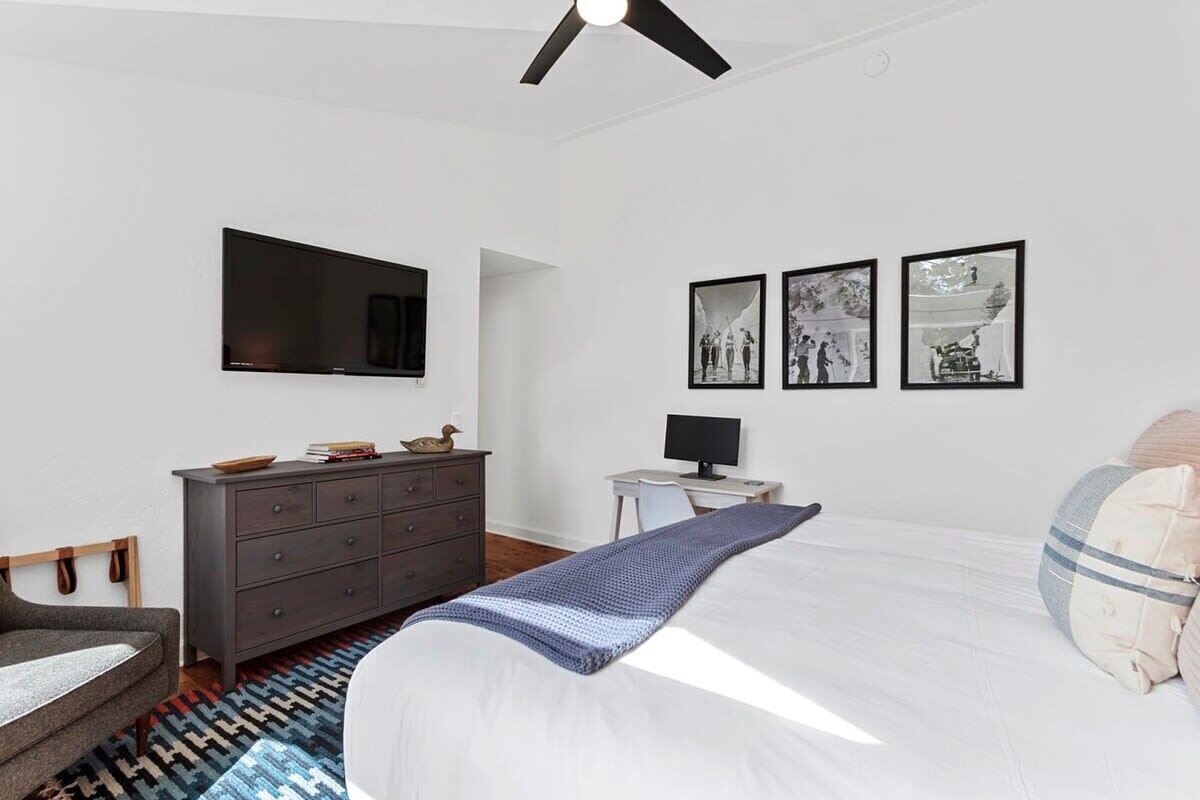 A bedroom with a bed, a dresser, a desk, a television, and framed pictures on the wall.