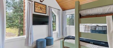 A bunk bed room with a television, curtains, and a framed picture on the wall.