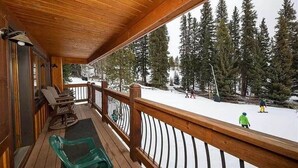 Une terrasse en bois dotée d’une rambarde, qui offre une vue sur un paysage enneigé et boisé.