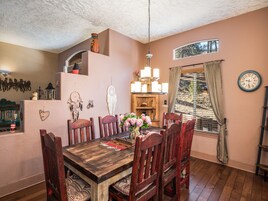Un comedor con una mesa y sillas de madera, una araña y un ventanal con cortinas.