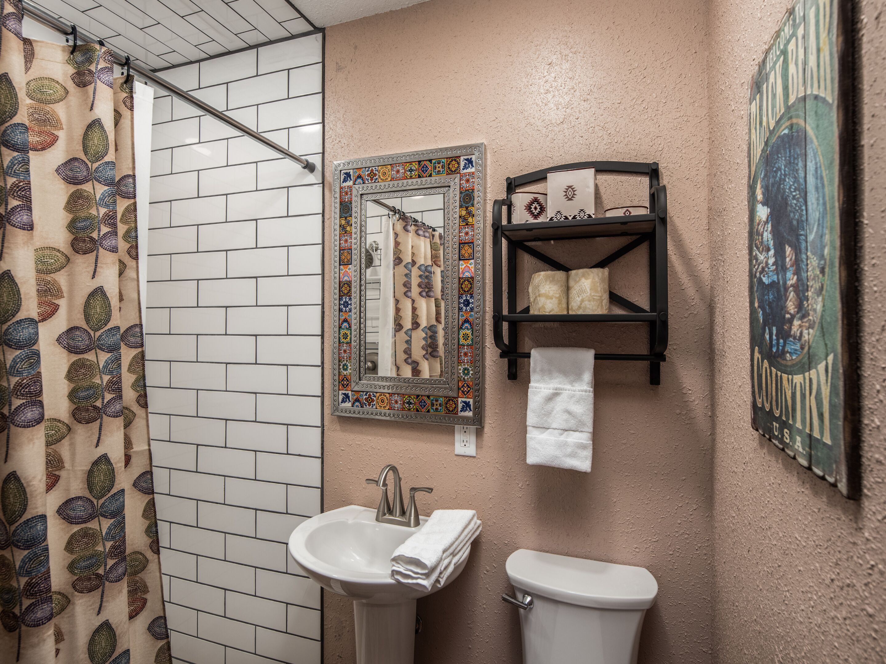 A bathroom with a shower, sink, toilet, decorative mirror, and towel rack.