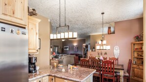 A kitchen with wooden cabinets, a granite countertop, and a dining area with wooden chairs and a table. - Casa Escondida by Ruidoso Vacation Rentals (Alto)