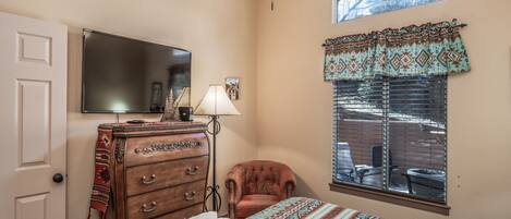 A bedroom with a bed, a dresser, a chair, a television, a window with blinds, and a ceiling fan.