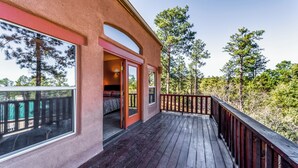 A wooden deck with a railing, a bedroom with a window, and a view of trees. - Casa Escondida by Ruidoso Vacation Rentals (Alto)