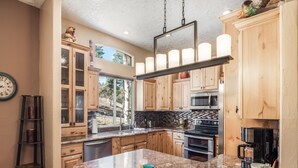 A kitchen with wooden cabinets, a granite countertop, a stainless steel refrigerator, and a large window. - Casa Escondida by Ruidoso Vacation Rentals (Alto)