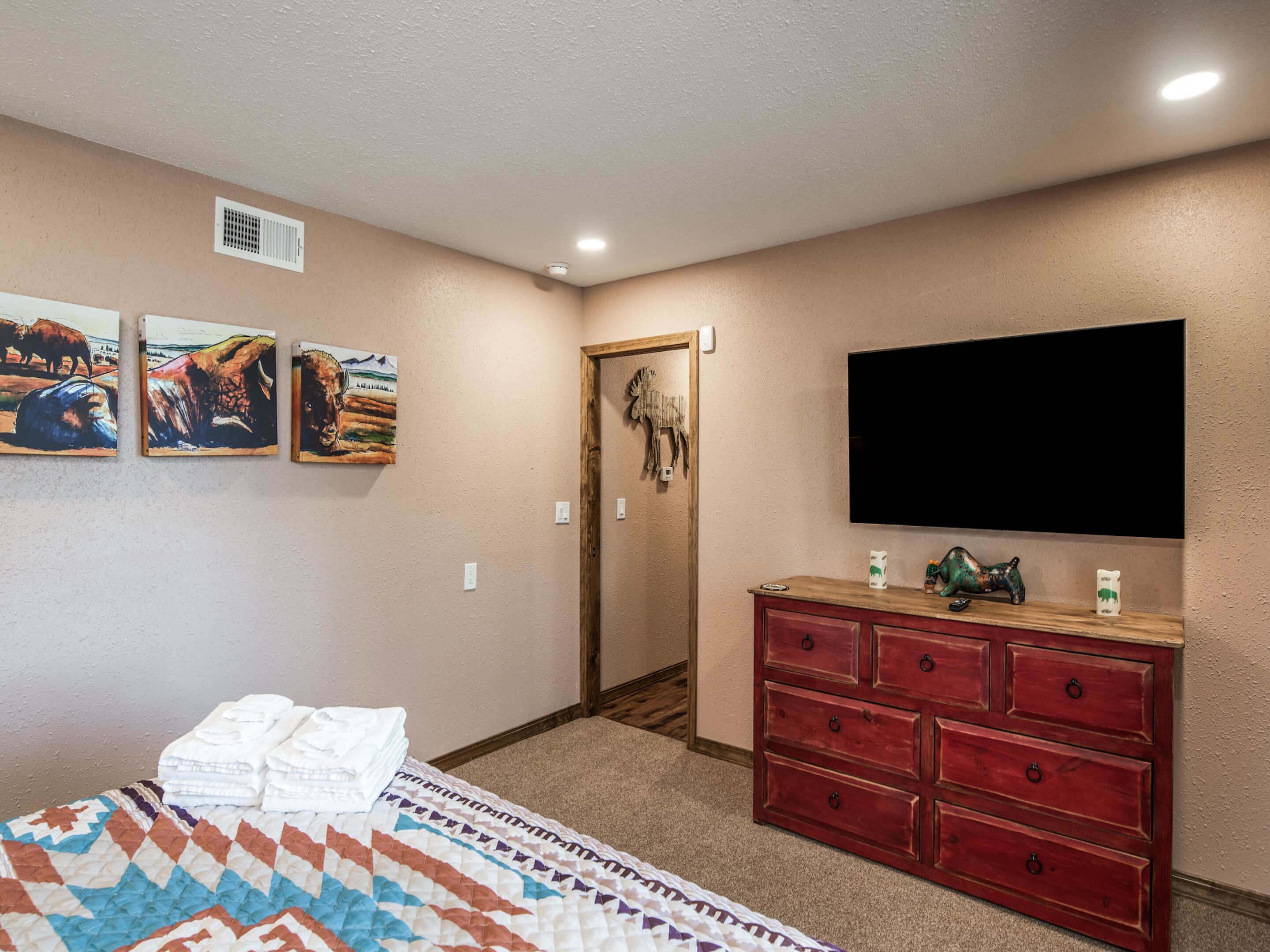 A bedroom with a bed, a dresser, a television, and three paintings on the wall.