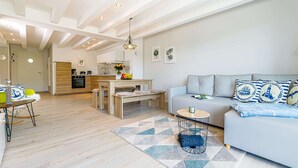 En moderne stue med sofa, spisebord og et køkken i baggrunden.