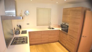 Una cocina compacta con estufa a gas, armarios de madera, campana extractora de acero inoxidable y una ventana con persianas.