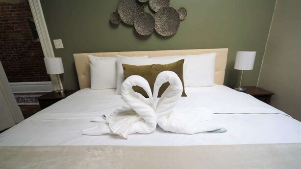 A neatly made bed with a unique towel arrangement, a headboard, and a decorative wall piece. - *Historic Gem* Heart of Southside-Sleeps 10 (Pittsburgh)