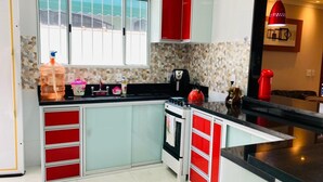 A kitchen with red and white cabinets, a stove, and a large window with a view of the beach. - Modern and cozy house with fireplace and heated pool just 50m from the beach. (Imperador - Praia Grande)