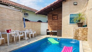 A swimming pool with a tiled deck, a lounge area with chairs, and a small table. - Modern and cozy house with fireplace and heated pool just 50m from the beach. (Imperador - Praia Grande)