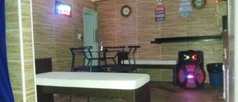 A room with a bench, a table, chairs, a neon sign, a clock, and a wall-mounted shelf.